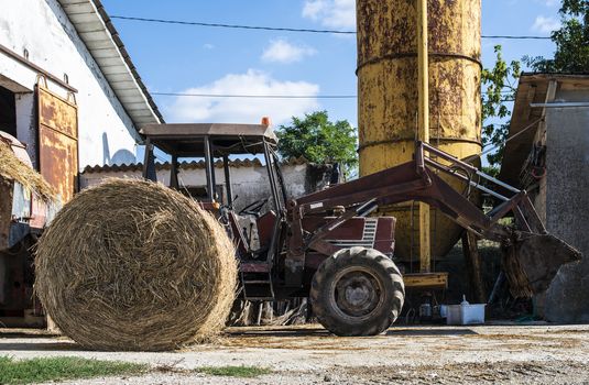 Tractor in farm. Bale hay in the foreground. Farming constructions.