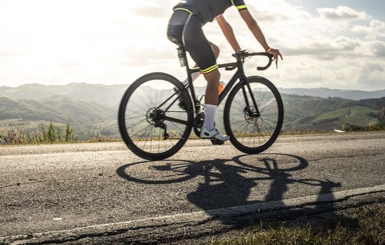 Cyclist sports on road. Sun Rays and shadows from the bike on the road. Outdoor cycling.