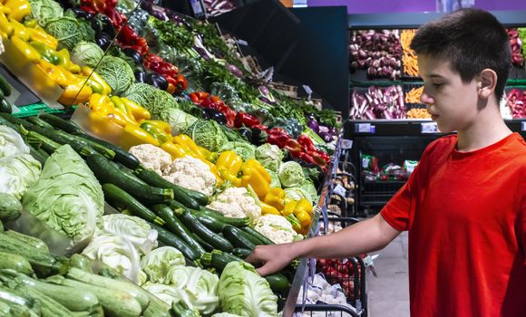 Child selecting vegetables on shelf in supermarket. Cabbage, zucchini, pepper and cauliflower.