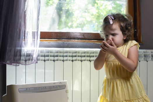 Little girl in a dusty room. Air purifier and coughing kid. Dust in the air. Allergy concept.