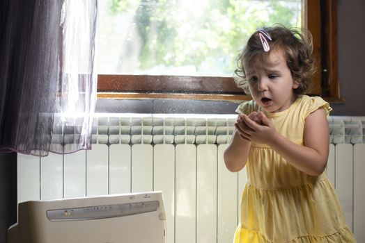 Little girl in a dusty room. Air purifier and coughing kid. Dust in the air. Allergy concept.