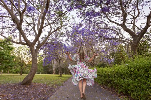 A joyful woman walks under a canopy of flowering Jacaranda trees in spring.  
Note: Some motion and movement in dress as she walks