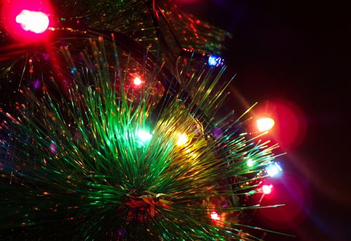 Christmas tree decorated with garland. Blurred background and glare from the lights of the garland. Christmas tree closeup.