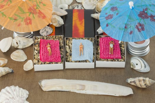 small miniature dolls are sunbathing in matchboxes under the parasol with shell around