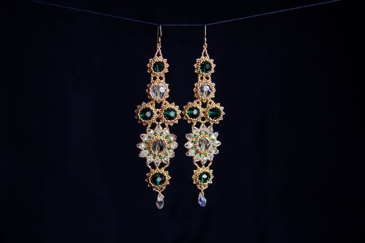 handmade jewelry made of beads in macro. earrings from white beads. earrings from stones. beautiful ornaments. earrings from golden beads. ornaments on a black background