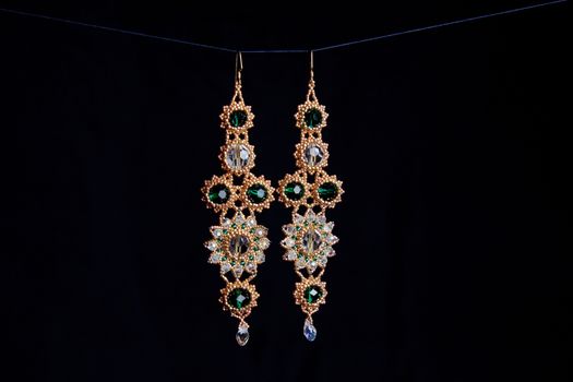 handmade jewelry made of beads in macro. earrings from white beads. earrings from stones. beautiful ornaments. earrings from golden beads. ornaments on a black background