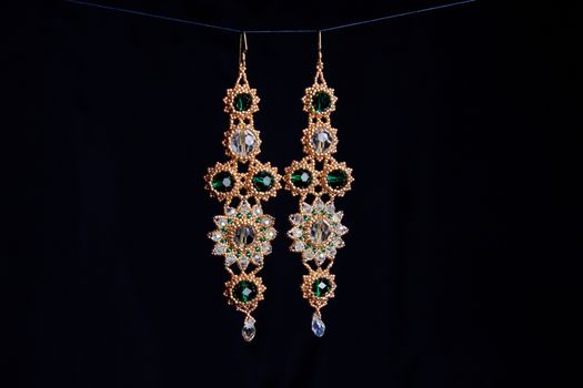 handmade jewelry made of beads in macro. earrings from white beads. earrings from stones. beautiful ornaments. earrings from golden beads. ornaments on a black background