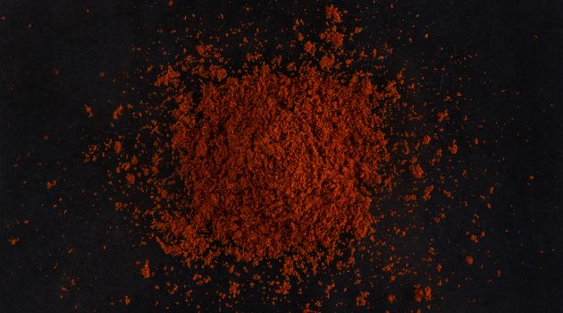 Pile of red paprika powder isolated on black background, top view