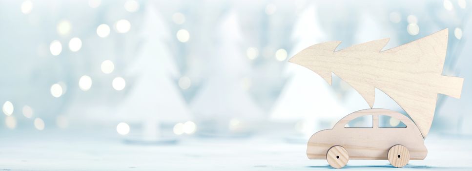 Wooden car carrying a christmas tree in front of dreamy and abstract glitter bokeh lights in forest background