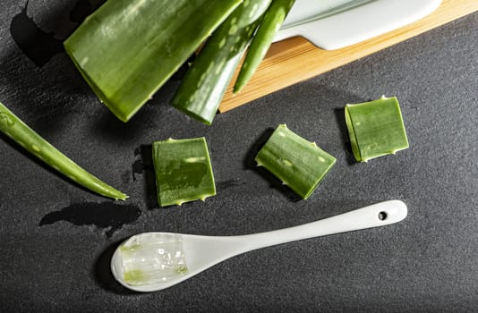 Aloe vera slices on dark background. Health and beauty concept. Closeup aloe pieces and spoon on backlight.