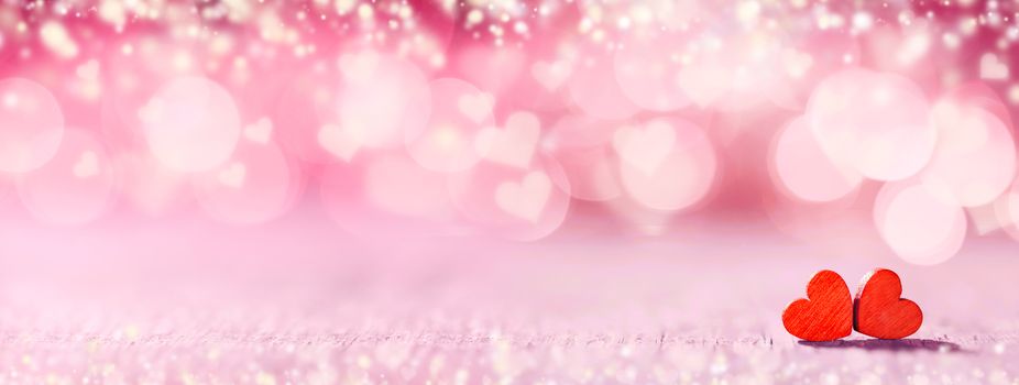 Two small handmade red wooden hearts on bright pink lights bokeh background Valentines day card