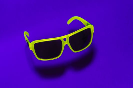 Bright green colour sun glasses in the air. Green floating in the air sunglasses on purple background. Lower shadow below the glasses. Minimalism summer concept.