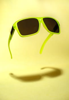 Bright green colour sun glasses in the air. Green floating in the air sunglasses on yellow background. Lower shadow below the glasses. Minimalism summer concept.