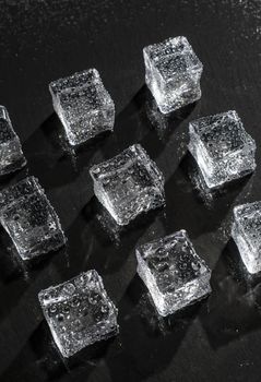 Ice cubes on black stone board. Wet ice cubes with water drops. Hard light. Deep shadows. Cold and freshness concept. Summer drinks conceptions. Dark background.