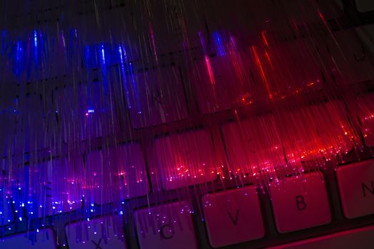 Colourful optic fibers illuminated on keyboard. High speed internet concept. Data transfer optic fiber cable. Bunch of many optical fibers, glowing different colors. Technology background.