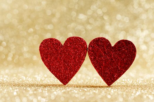 Two small handmade red glitter hearts on bright golden lights bokeh background Valentines day card