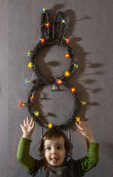 Little girl hold bunny easter decoration on wall. Flowers lights on bunny shape.