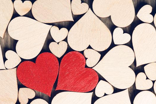 Two wooden painted red hearts among many colorless wooden hearts