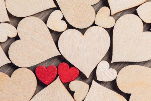 Two wooden painted red hearts among many colorless wooden hearts