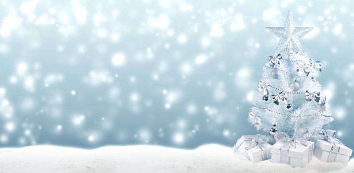 White christmas tree with silver decorations and gifts on snow on bokeh background