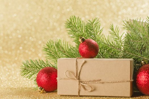 Christmas or new year decorations, craft paper gift box, fir tree branches on golden glitters background, copy space