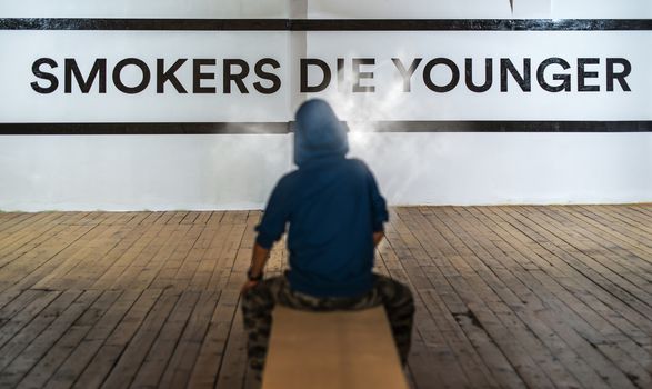 Teenager smoking and message on wall - Smokers die younger. No smoking concept with child. Casual clothes.