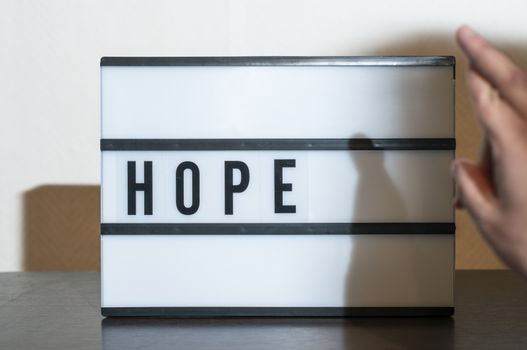 Text hope nad crossed fingers. Concept for hope,  salvation and luck. White illuminated board.