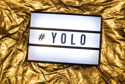 Text YOLO on white illuminated board. You only live once concept and hashtag. Yellow shiny background.