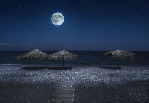 Straw umbrellas on the beach in the night. Moonlight on sea. Night starry sky. 