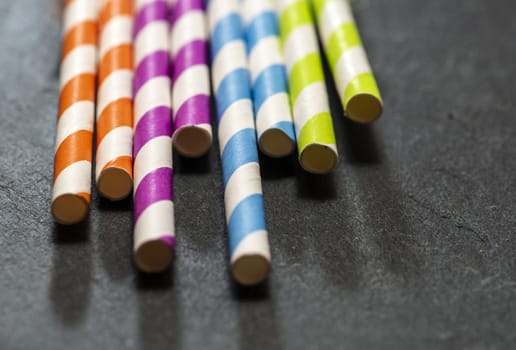 Multicoloured drink straws on dark stone background. Vibrant colours contrast on natural light. Paper made straws. Close-up macro shot.