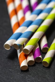 Multicoloured drink straws on dark stone background. Vibrant colours contrast on natural light. Paper made straws. Close-up macro shot.