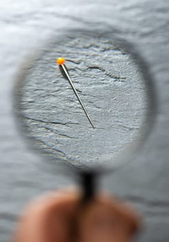 View small Needle through magnifying glass on a dark background. Concept for searching and finding small object with magnifying glass. Tailor's pin.