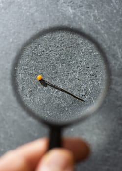 View small Needle through magnifying glass on a dark background. Concept for searching and finding small object with magnifying glass. Tailor's pin.