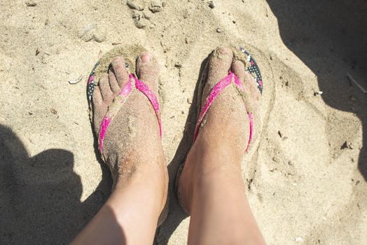 Woman feet with flip flops on the sand. Sunny day