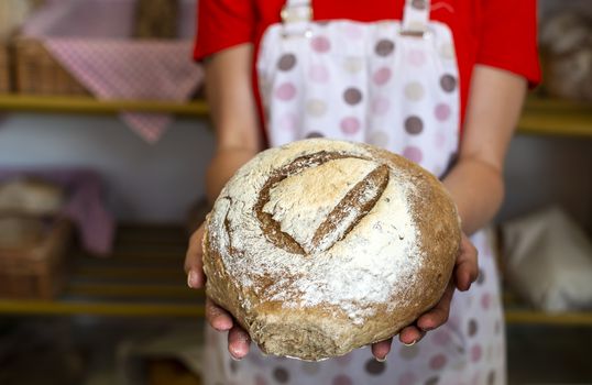 Woman in apron shows bread in a bakery. 