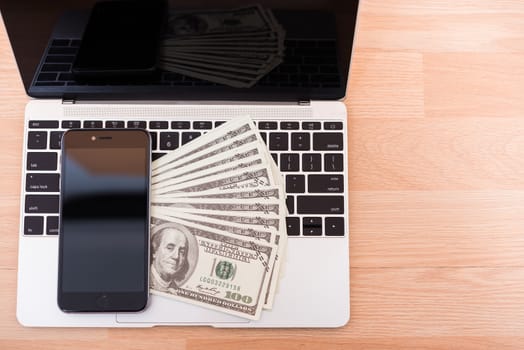 Top view laptop computer, dollar bill and smartphone blank screen on keyboard at office desk table, finance concept