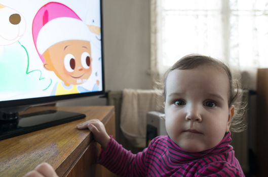 Baby girl watch TV. In fron of the TV.