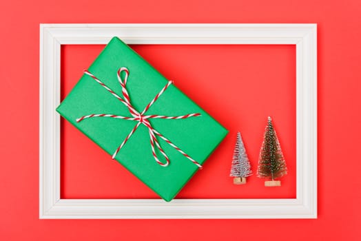 New Year, Christmas Xmas holiday composition, Top view both green fir tree branch and green gift box in frame on red background with copy space
