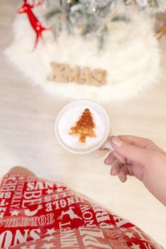 Festive woman holds a cappuccino with festive Christmas tree design of chocolate on milk froth