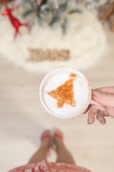 Woman holding a cappuccino with Christmas tree design on milk froth at Christmas time.Shallow depth of field suitable for text overlay