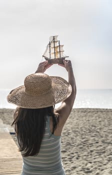 Woman with hat hold boat model on the beach