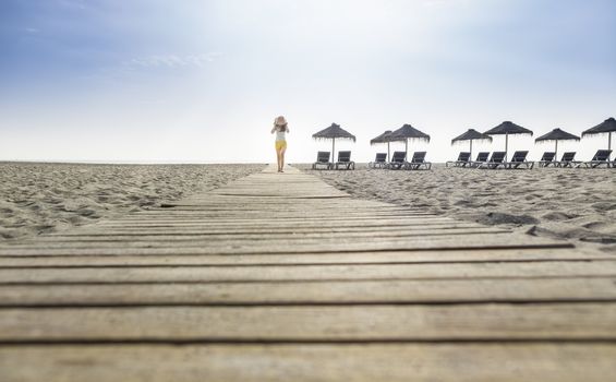 Woman with hat on wooden trail on the beach in the morning. Sunrise