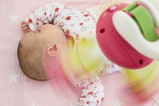 Baby girl in a bed with toys around. Pink tones