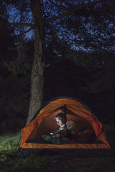 Man watching his smartphone in a tent at night.