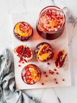 Winter sangria on white marble background. Jugful of sangria and glasses with orange slice and pomegranate. Vertical. Top view or flat lay.