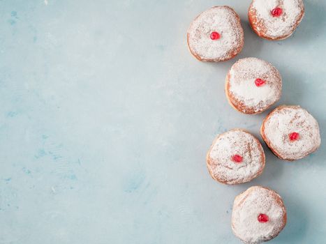 Hanukkah food doughnuts with jelly and sugar powder on blue background. Jewish holiday Hanukkah concept and background. Copy space for text. Top view or flat lay.