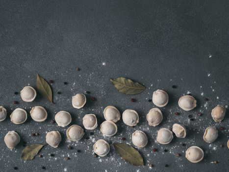 Pattern of frozen uncooked russian pelmeni with peppercorns and bay leaves on black background. Creative layout of dumplings. Beautiful scattered raw dumplings. Top view, flat lay. Copy space for text