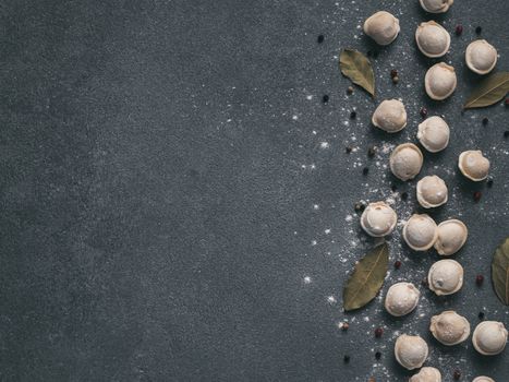 Pattern of frozen uncooked russian pelmeni with peppercorns and bay leaves on black background. Creative layout of dumplings. Beautiful scattered raw dumplings. Top view, flat lay. Copy space for text