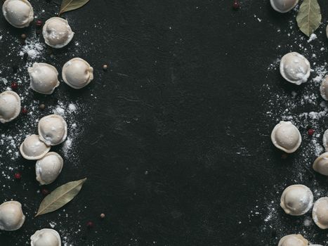 Pattern of frozen uncooked russian pelmeni with peppercorns and bay leaves on black background. Creative layout of dumplings. Beautiful scattered raw dumplings. Top view, flat lay. Copy space for text