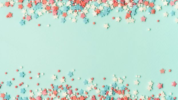 Festive border frame of colorful pastel sprinkles on blue background with copy space in center. Sugar sprinkle dots and stars, decoration for cake and bakery. Top view or flat lay. Banner